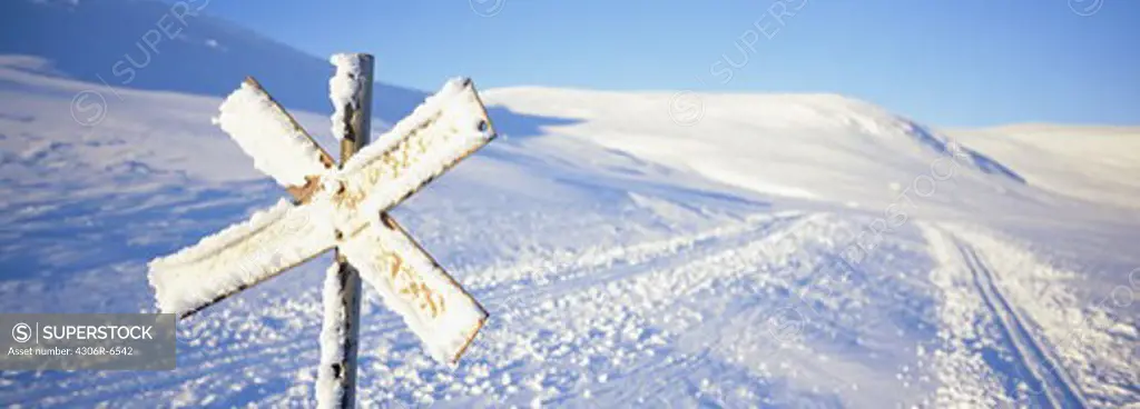 Snow covered road sign with cross country skiing track in background