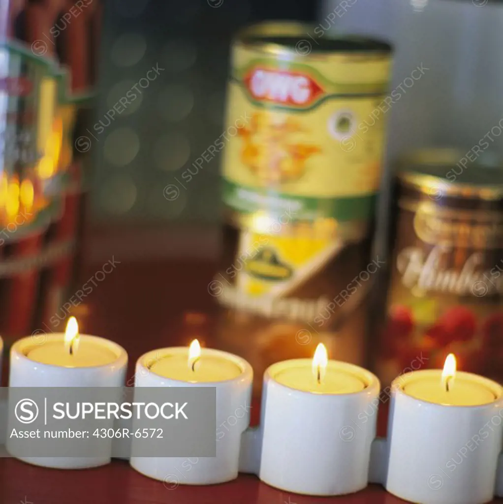 Row of illuminated candles with canned food in background