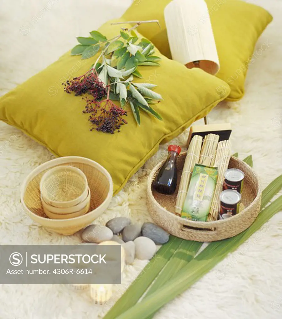 Spa oils in basket with candles and pebbles, plant on pillow in background