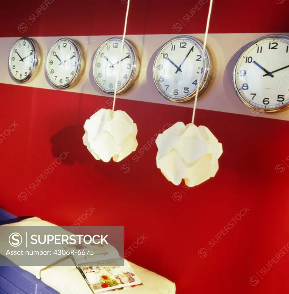 Lamps hanging in front of rows of clocks on red wall