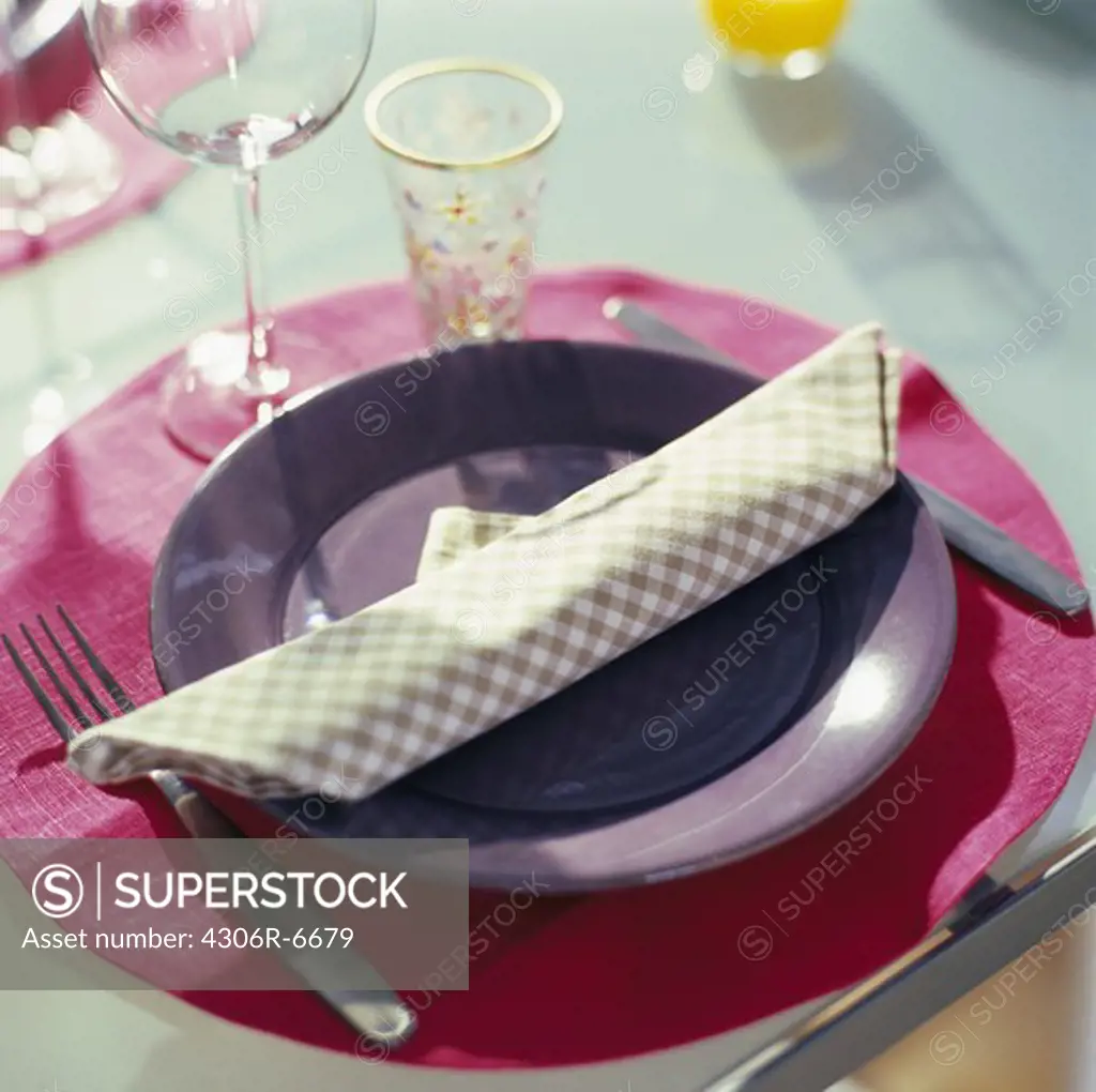 Rolled up napkin on plate, cutlery and glasses on side