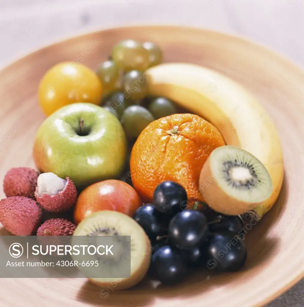 Variety of fruits including kiwi, grapes, litchi, orange, apple and banana on plate