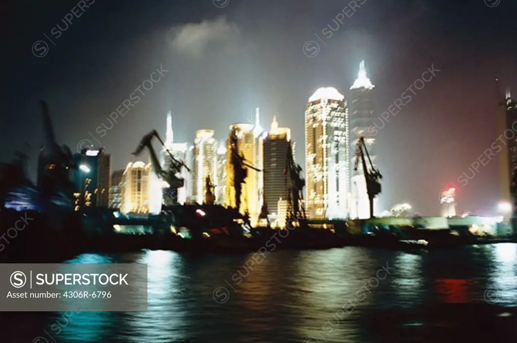 Illuminated buildings in city at night, sea in foreground