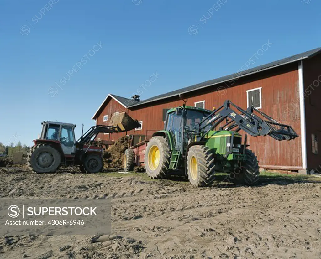 Tractors in agricultural field beside red barn building