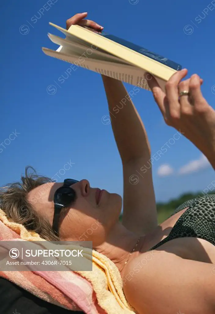 Woman lying on beach reading book, close-up