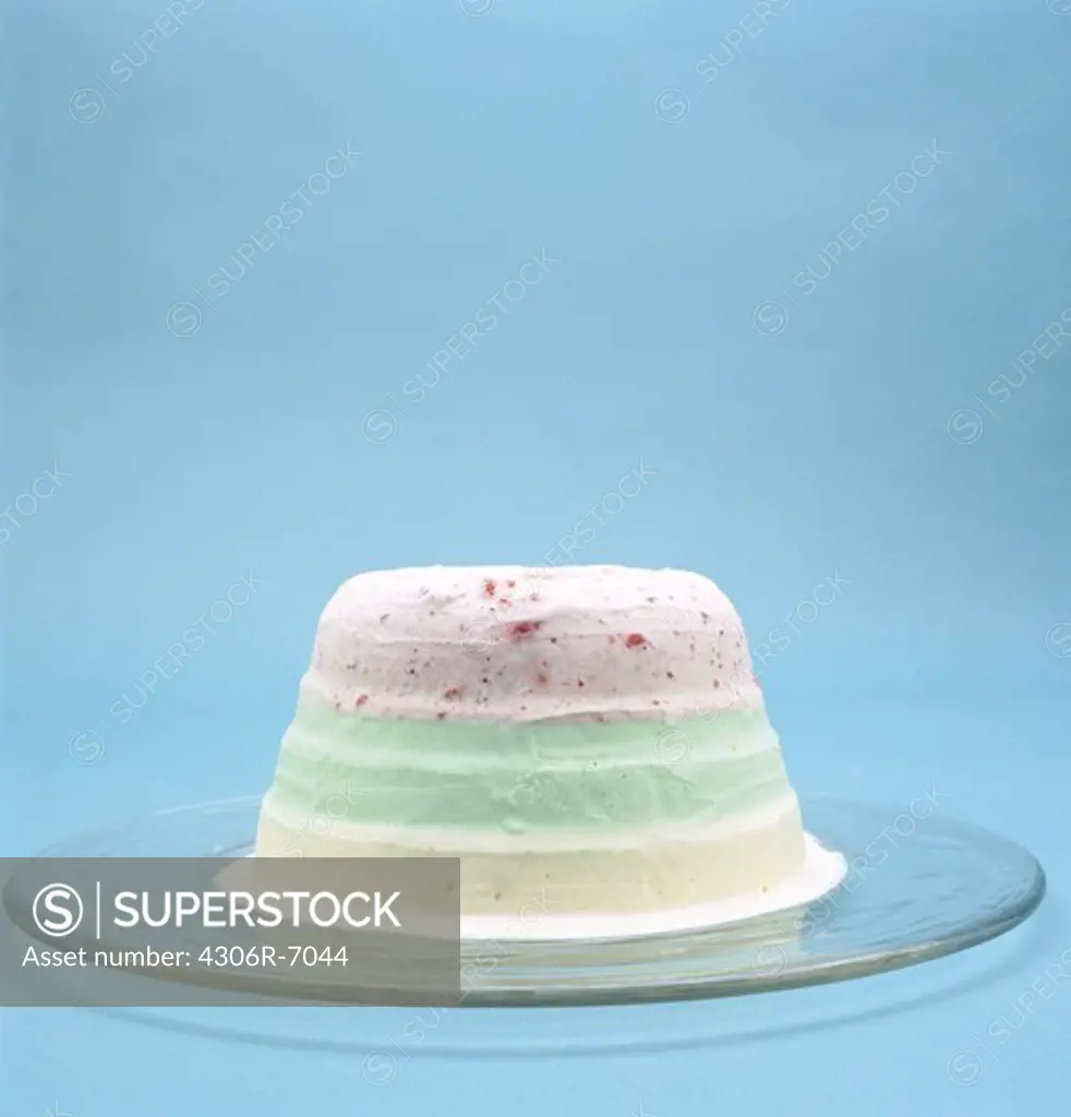 Multicolored ice cream cake on serving dish against blue background