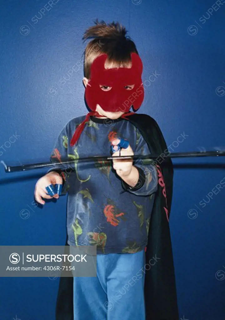 Boy wearing mask and cloak standing against white background