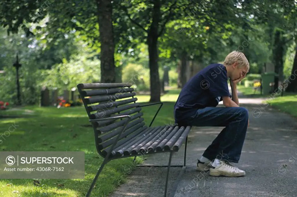 Teenage boy sitting on park bench with head in hands