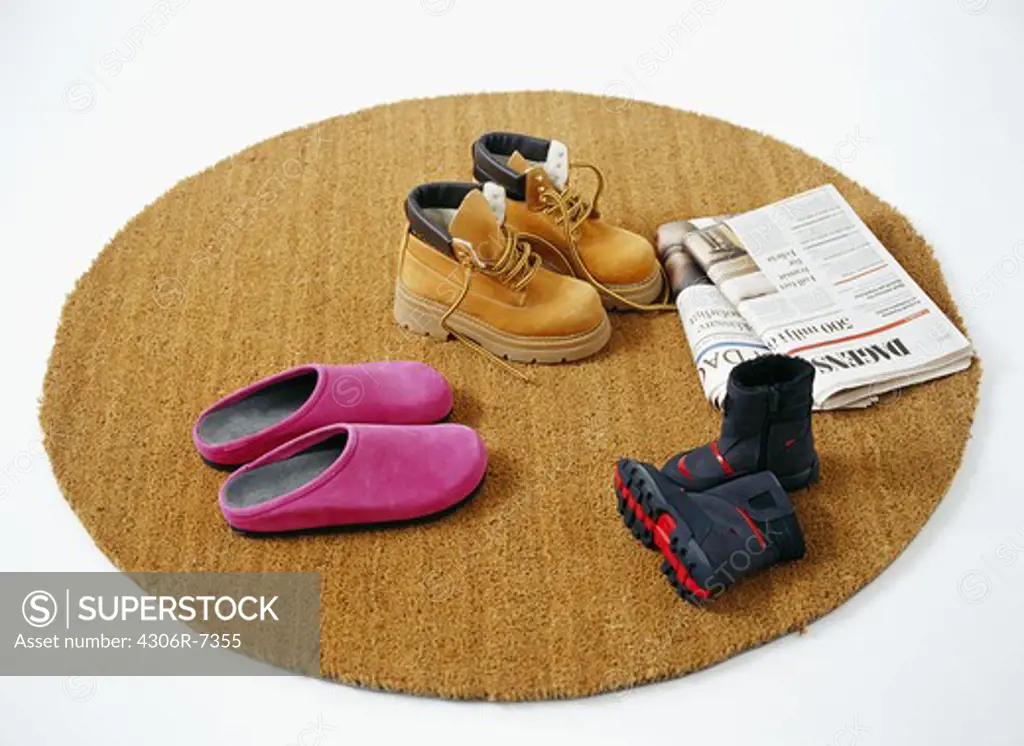 Three pairs of children's footwear with folded newspapers on round carpet