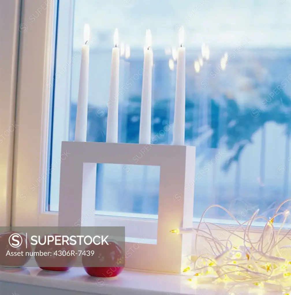 Artificial red apples with row of lighted candle on window sill at Christmas