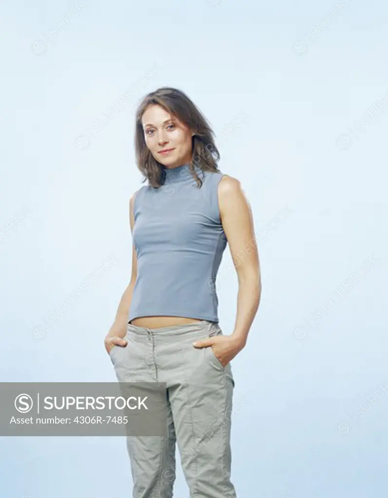 Portrait of mid adult woman standing with hands in pockets against blue background