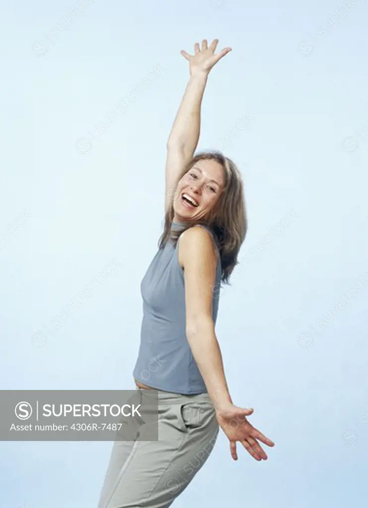 Happy mid adult woman standing with arms up against blue background