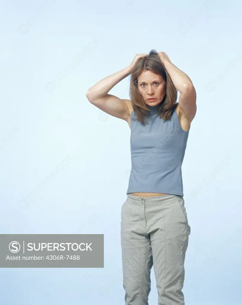 Confused mid adult woman standing with hands in hair against blue background