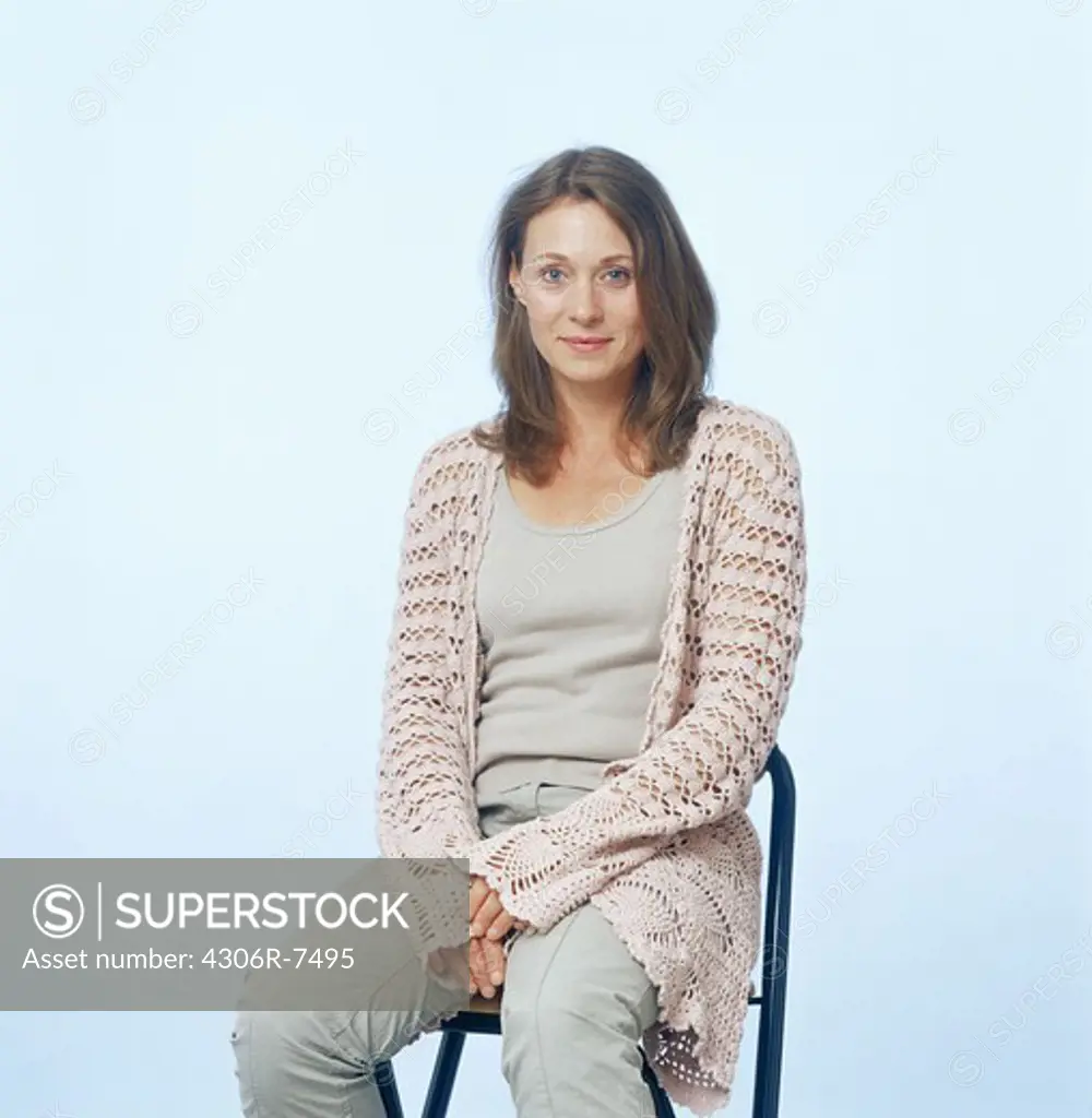 Portrait of mid adult woman sitting on chair against blue background