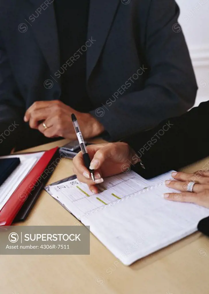 Business people sitting at desk writing on diary