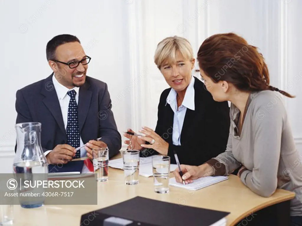 Businessman and women sitting at desk having discussion, smiling