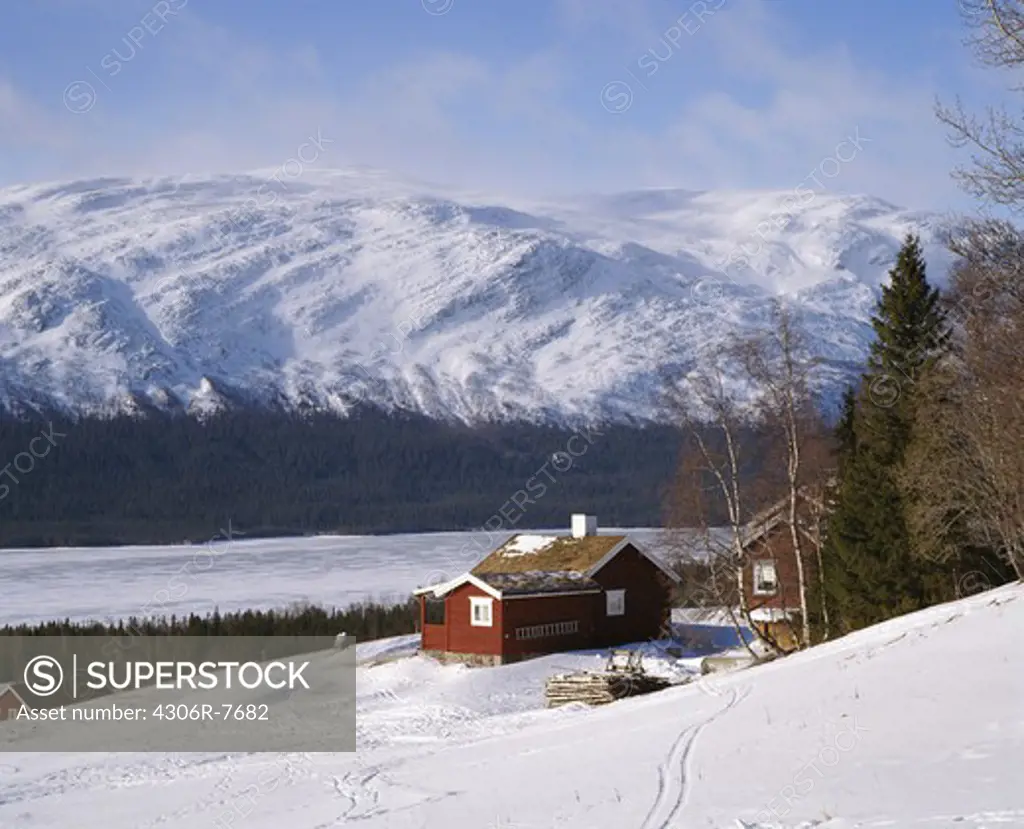 Wooden cottage in snow covered landscape with mountains in background