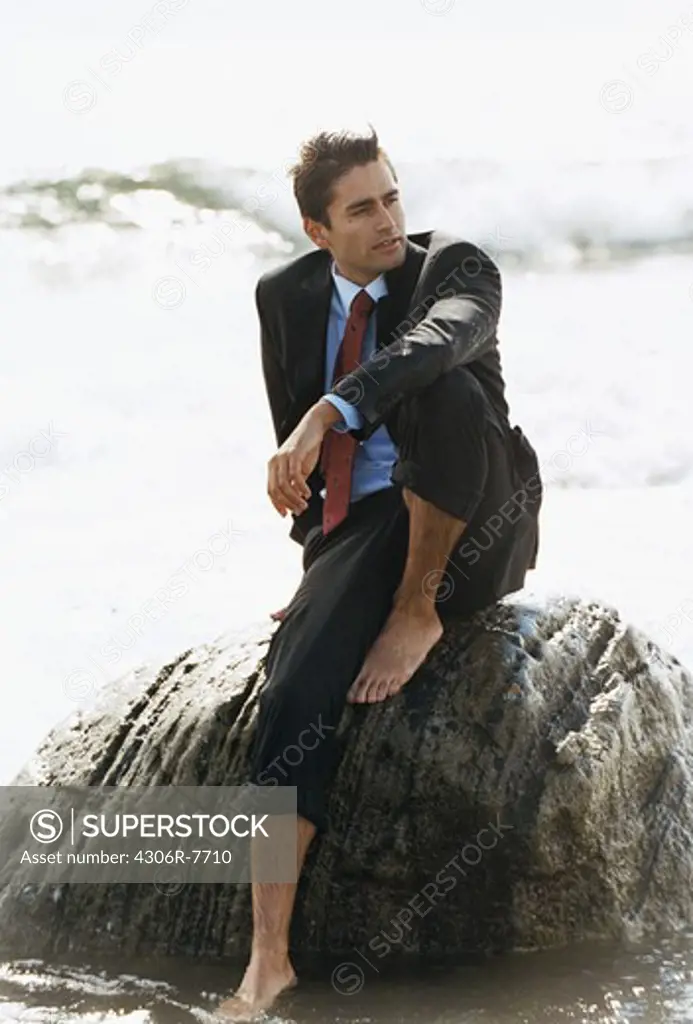 Barefoot businessman sitting on rock in sea