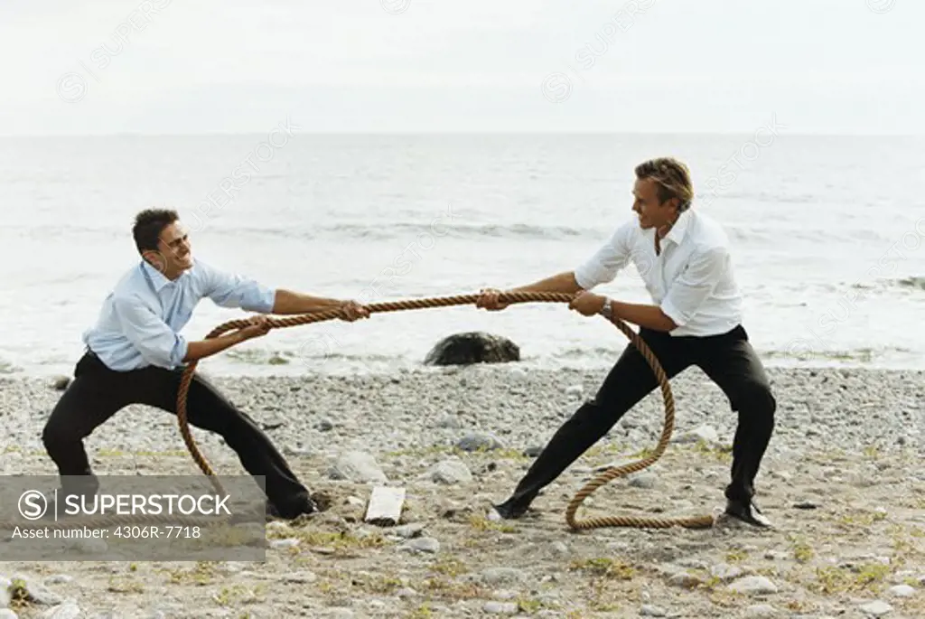 Two businessmen playing tug of war in beach