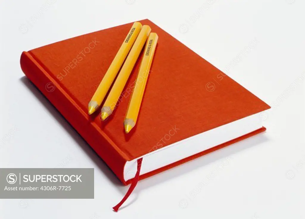 Three pencils on top of red notebook, close-up