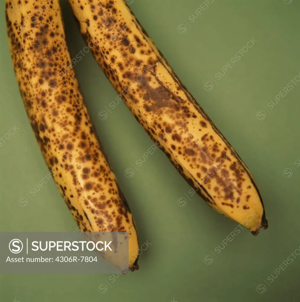 Two bruised bananas against green background, close-up