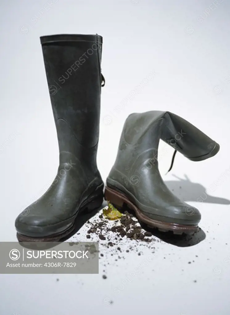 Pair of dirty wellington boots with soil against white background