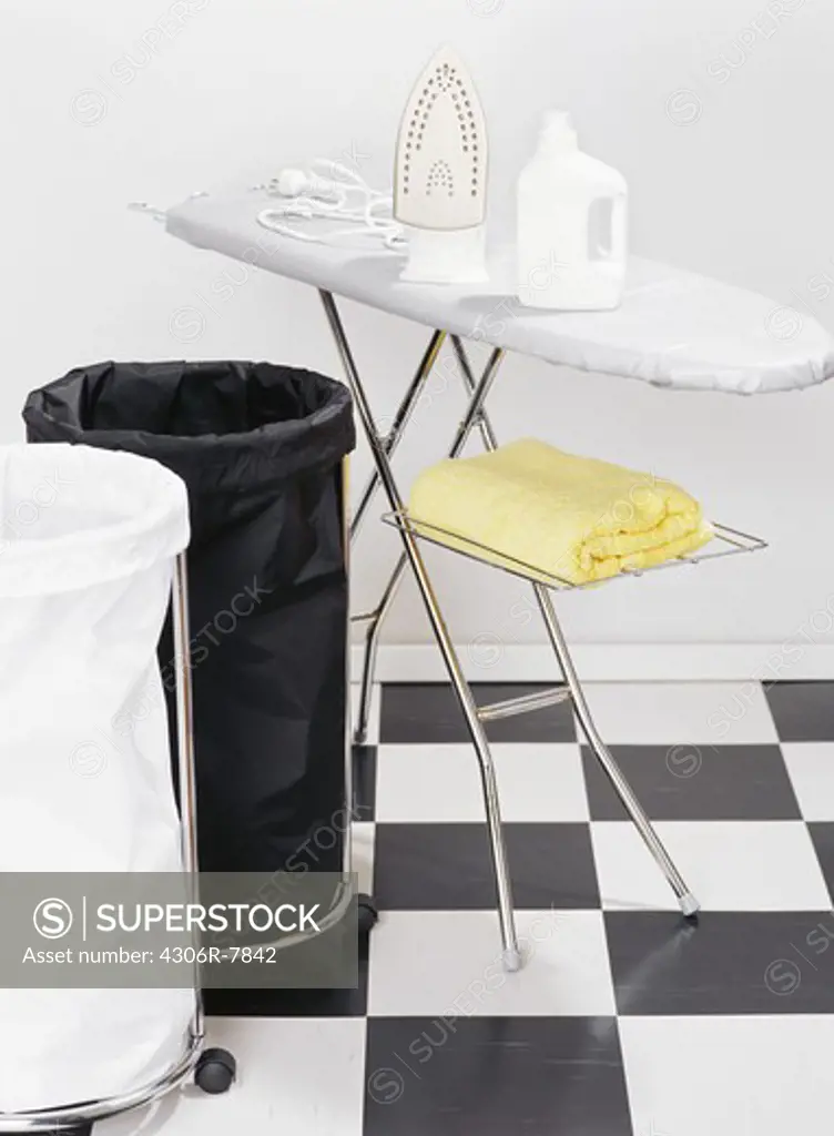 Ironing board on checked floor, black and white laundry baskets on side