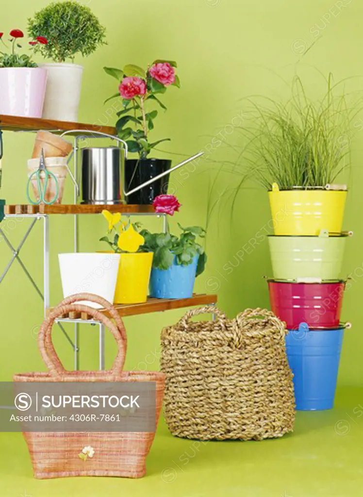 Woven baskets, stack of multicolored pot plants, and rack with potted flowers against green background