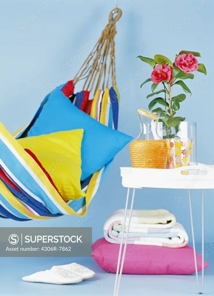 Brightly coloured hammock with pillows, table with vase of flower on side and folded blanket on floor