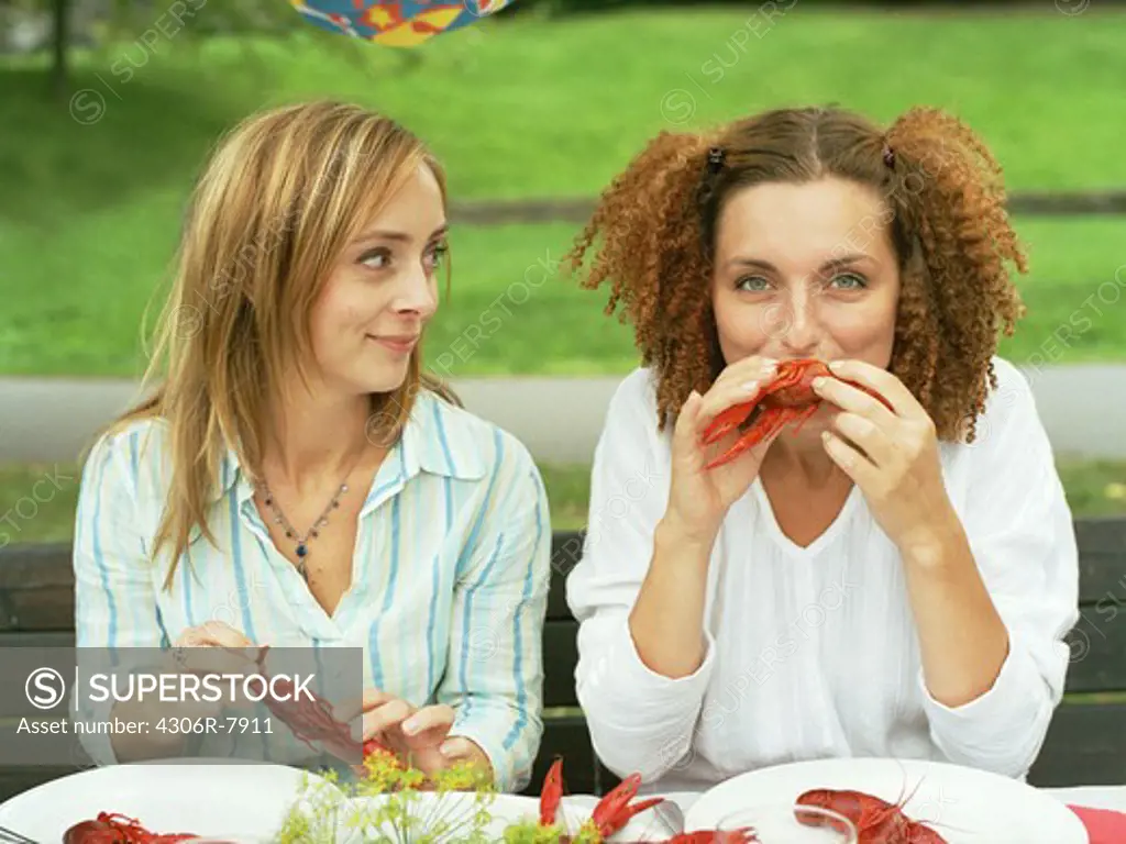 Two women sitting at table eating crayfish