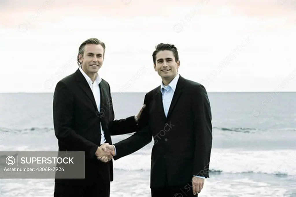 Portrait of two businessmen shaking hands with sea in background