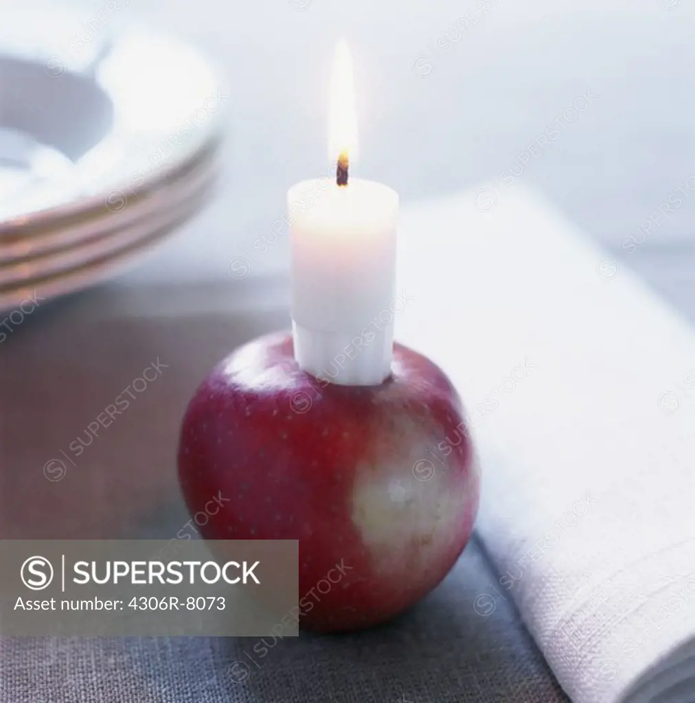 Burning candle on top of apple placed on wooden surface, close-up