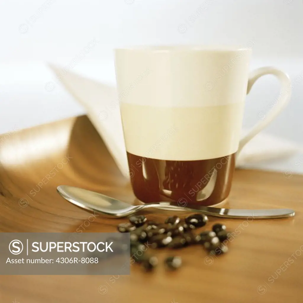 Coffee beans, spoon and cup on wooden surface