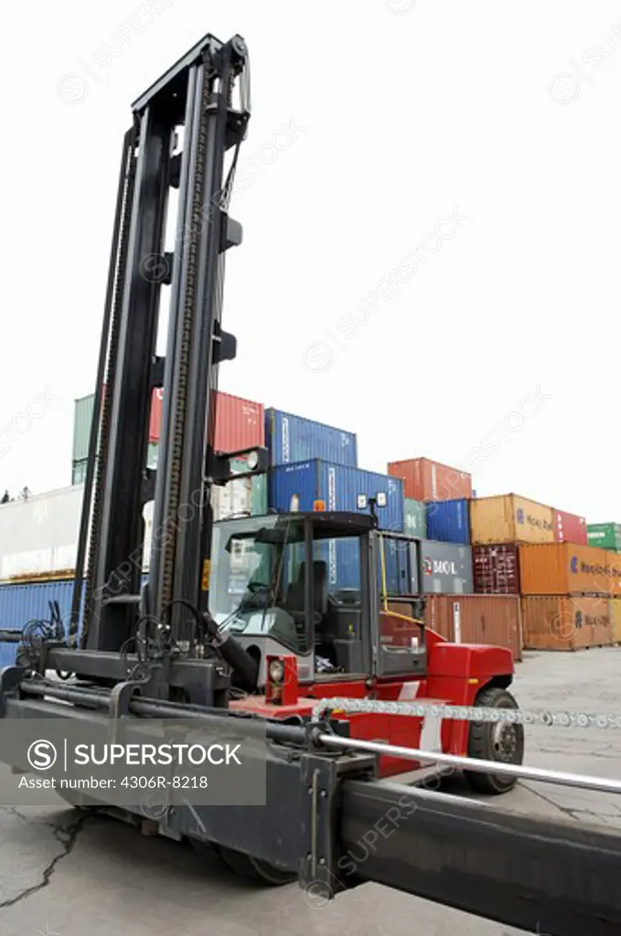 Red forklift truck with pile of big metal goods containers