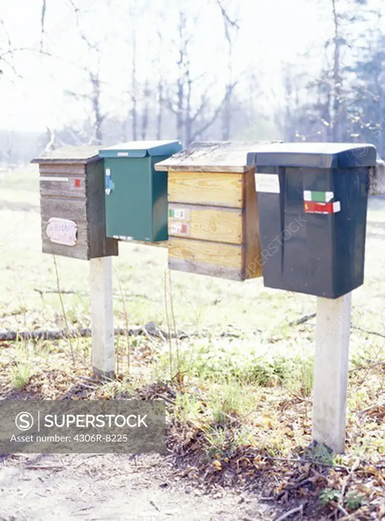 Four different letterboxes next to each other with grass and vegetation in background