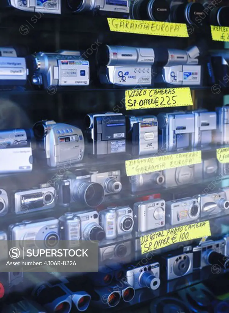 Glass showcase displaying different types of cameras and binoculars with prices