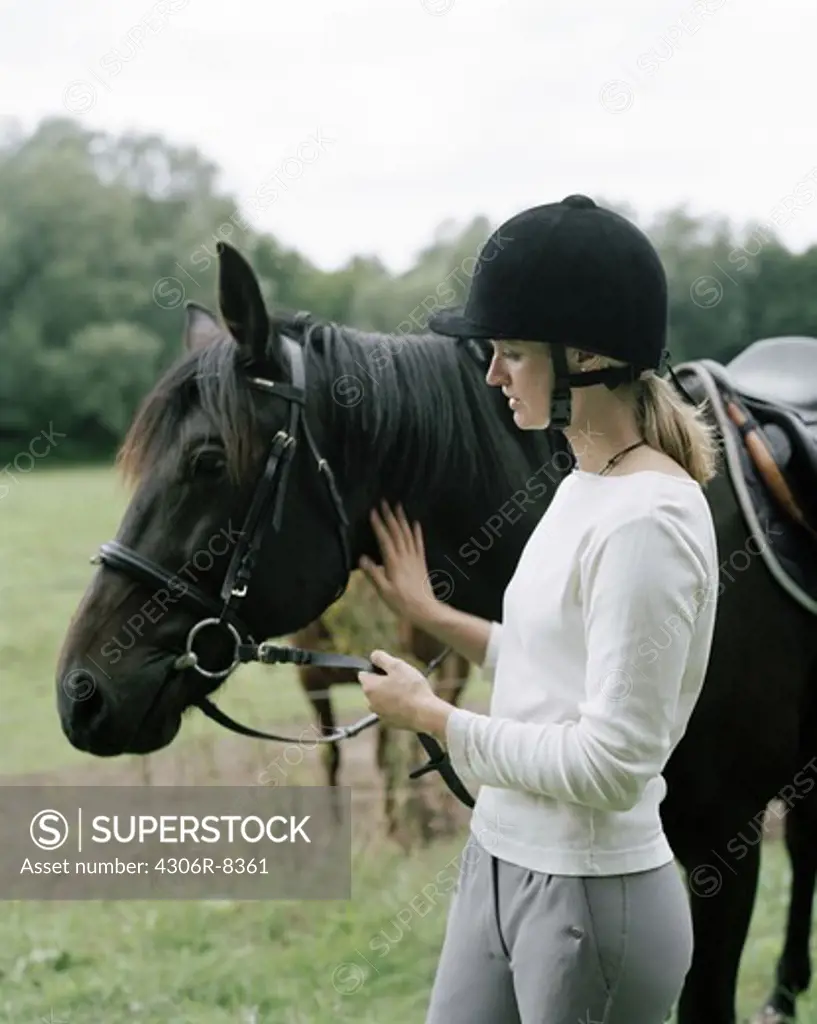 Woman wearing riding helmet stroking horse