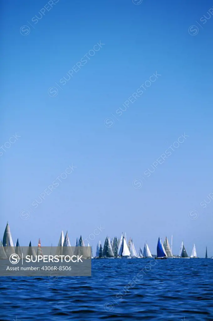 Large group of sailing boats in sea against blue sky