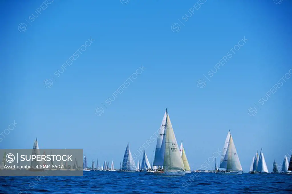 Large group of sailing boats in sea against blue sky