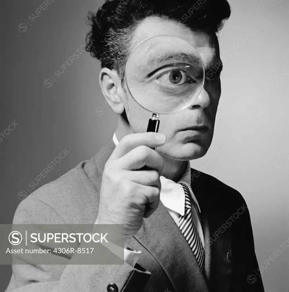 Man holding magnifying glass in front of eye
