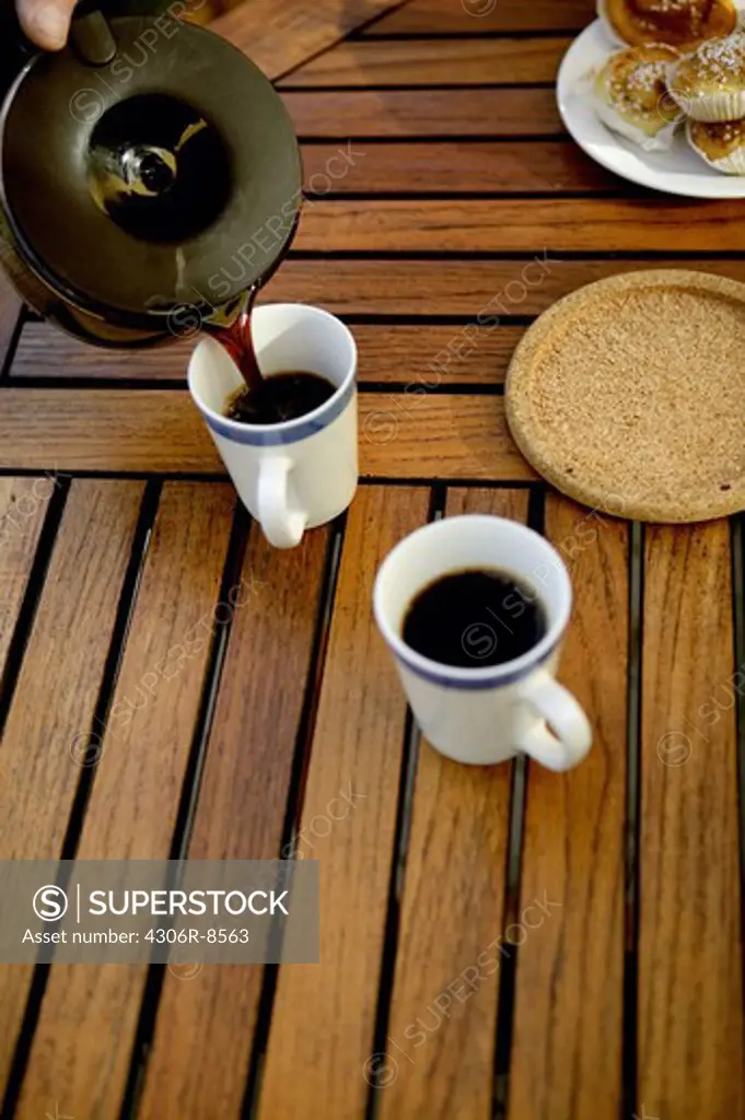 Person pouring coffee into cups placed on wooden table