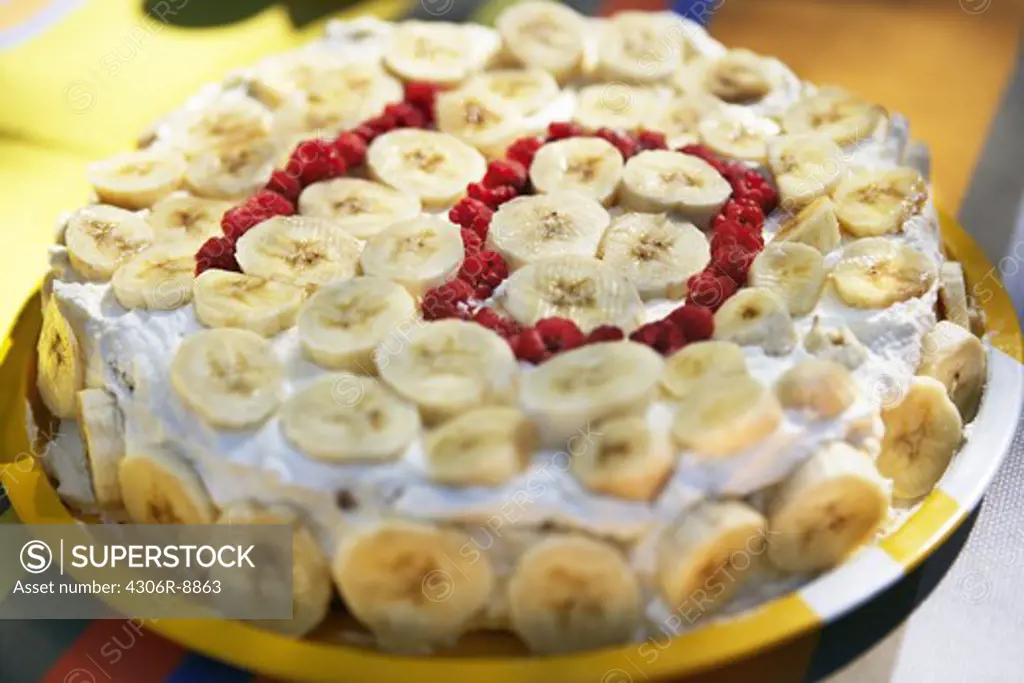 A cake with banana slices and 10 written with berries.
