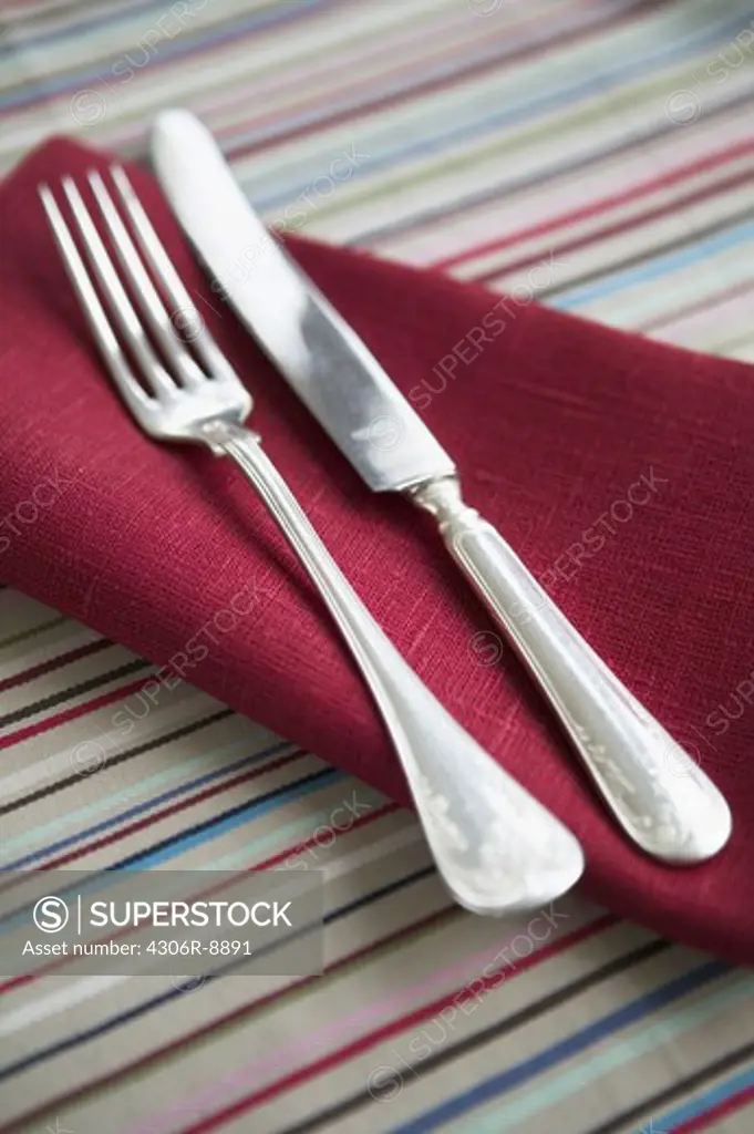 A silver knife and fork on a napkin, close-up.