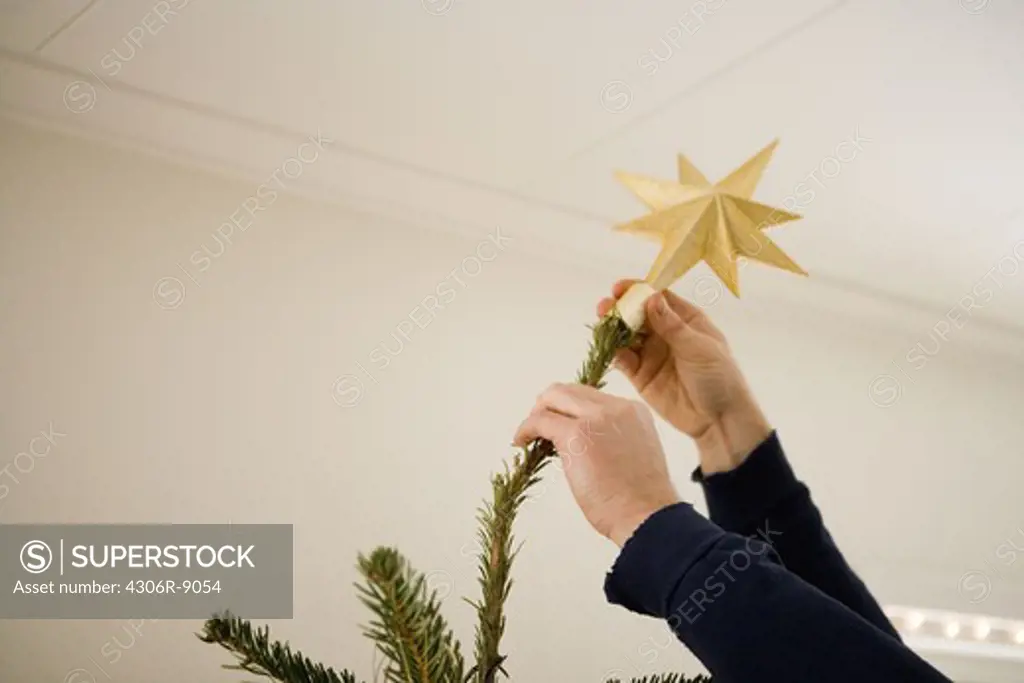 A Christmas star being put on a Christmas tree.