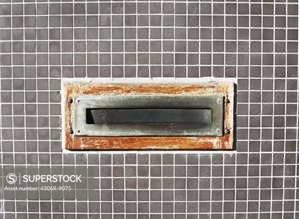 A worn letterbox on a checked wall.