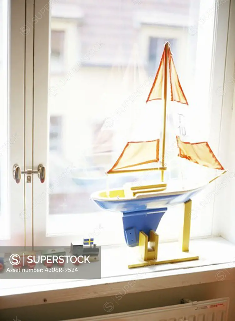A toy boat and a toy train in a window.