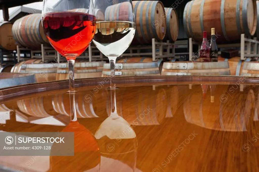 Two glasses of wine on a table, with wine barrels in the background.