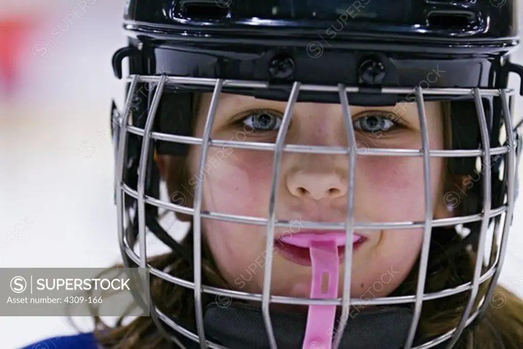 A little girl wearing a hockey helmet and mouthguard.