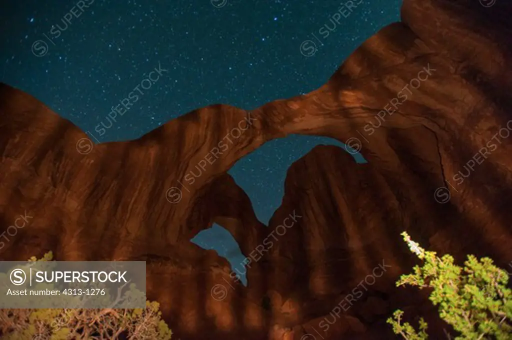 Double Arch is lit up using light-painting at night with the star-filled night sky overhead in Arches National Park, Utah.
