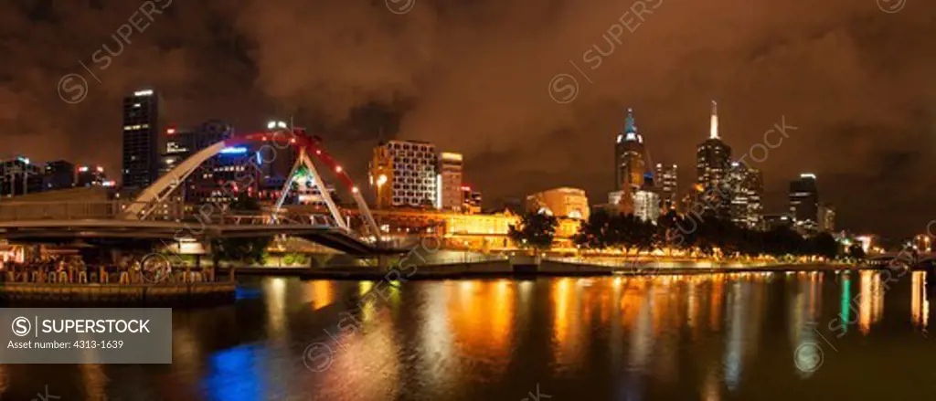 Australia, Victoria, Melbourne, Panorama of city skyline and southgate footbridge at night along Yarra River looking towards Federation Wharf from Southbank